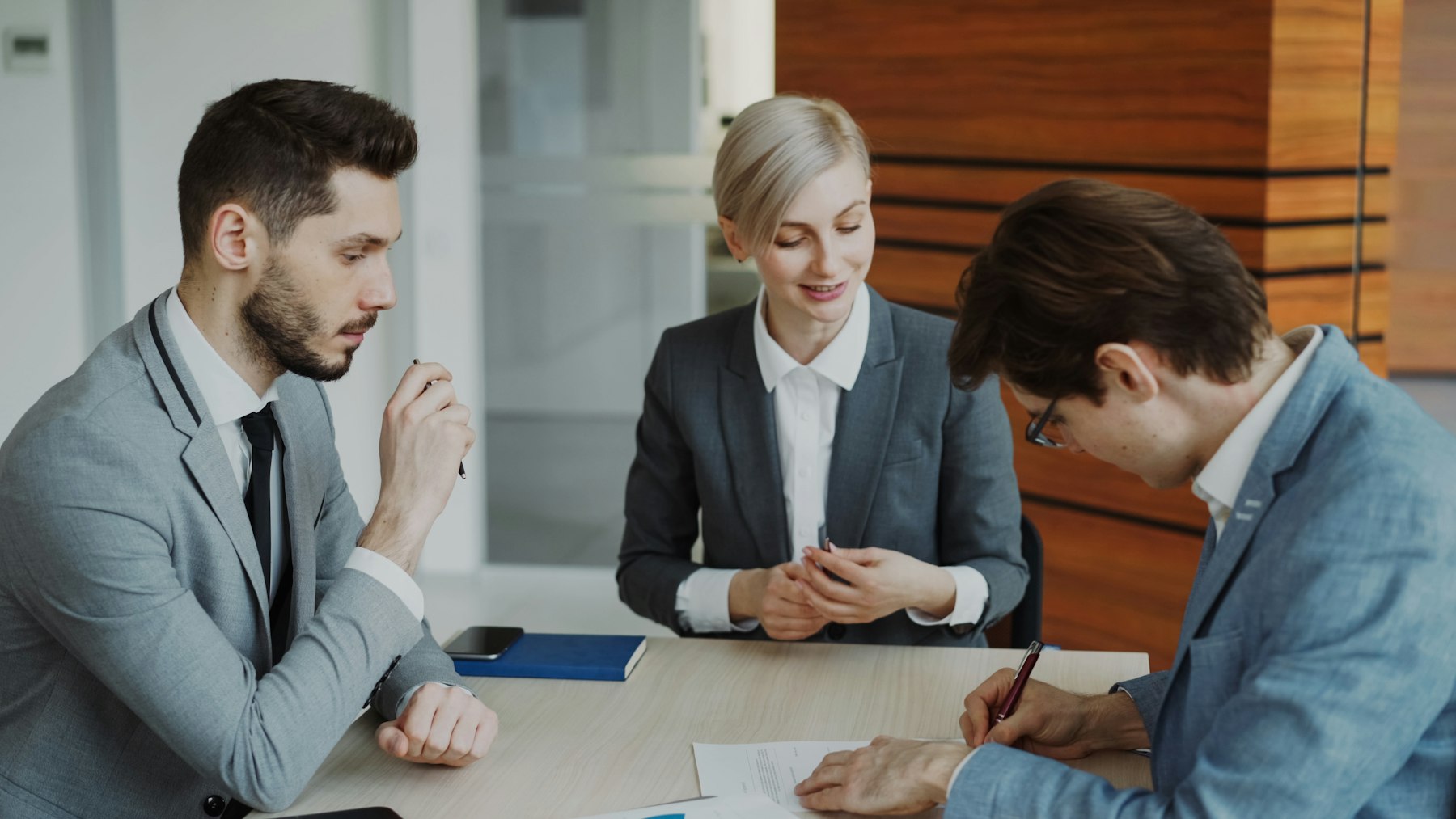 Two businesspeople reviewing and signing a contract at a table in a modern office
